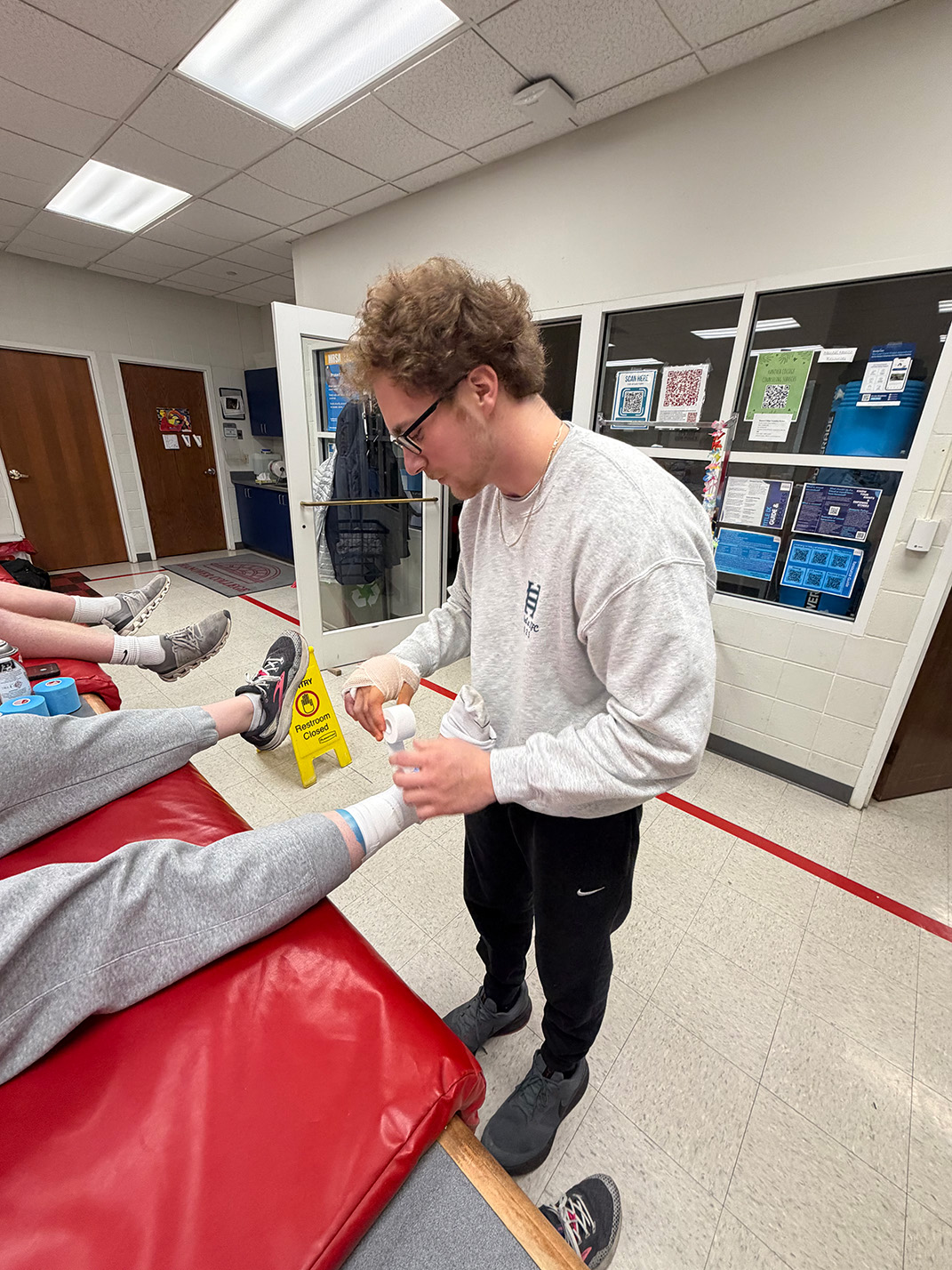 Photo of Eli Tackett, class of 2027, a white male with brown curly hair working on wrapping an ankle.