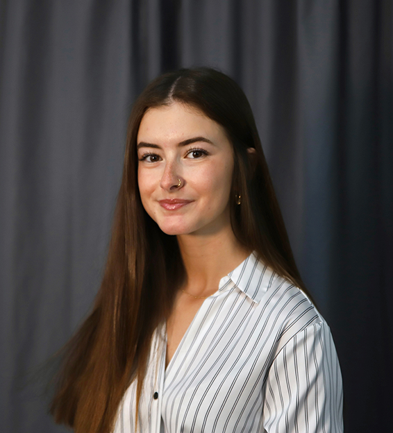 A photo of Emma Marzouk, a white female with long brown hair and wearing a white shirt with stripes.