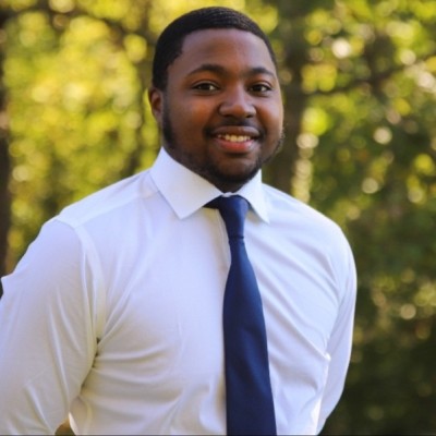 Photo of Talal Laguda, a black male wearing a white shirt and blue tie.